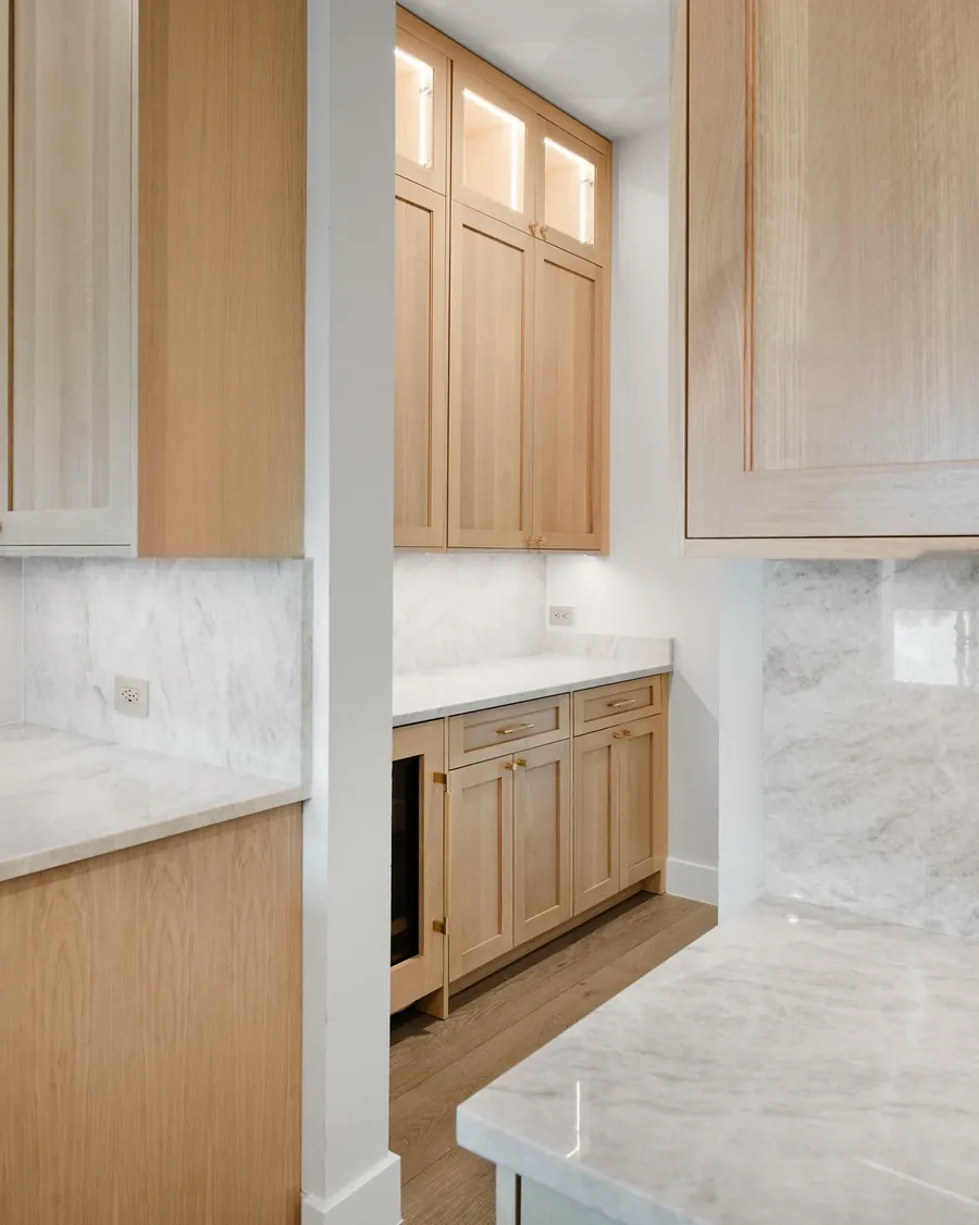 White oak butler pantry with marble counters, glass-front uppers and an undercounter fridge